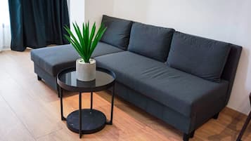 A modern living room with a grey sofa, a small black side table, and a potted plant.