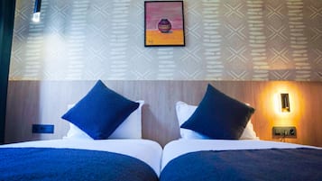 A double bed with dark blue bedding and pillows, a framed artwork above, and a wall-mounted light fixture.