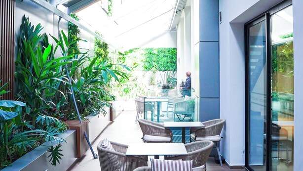 A modern outdoor patio area with wicker furniture, a glass table, and lush vertical gardens.