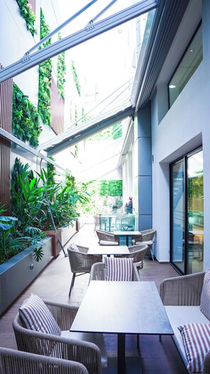 Un patio exterior moderno con mobiliario de mimbre, una mesa de vidrio y exuberantes jardines verticales.