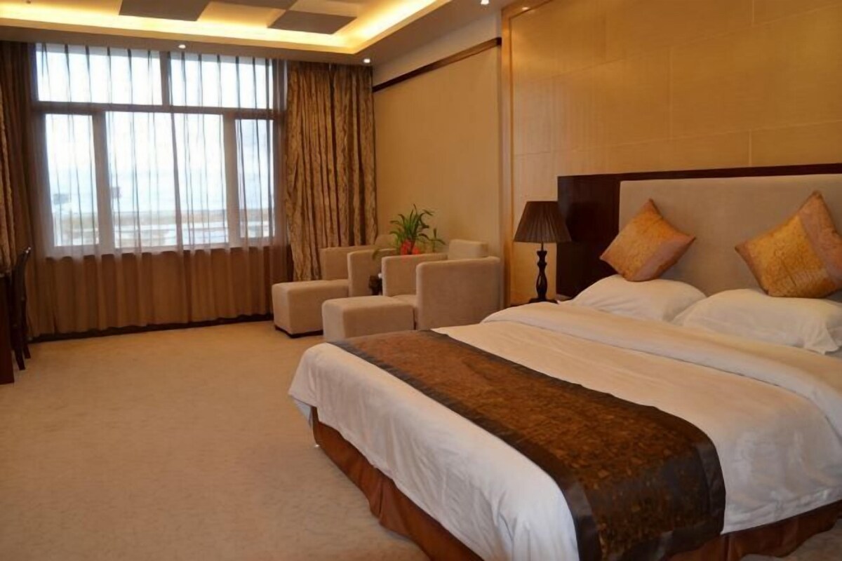 Ein Hotelzimmer mit einem großen Bett, einer Sitzecke mit Stühlen, einer Topfpflanze und Blick ins Freie durch das Fenster.