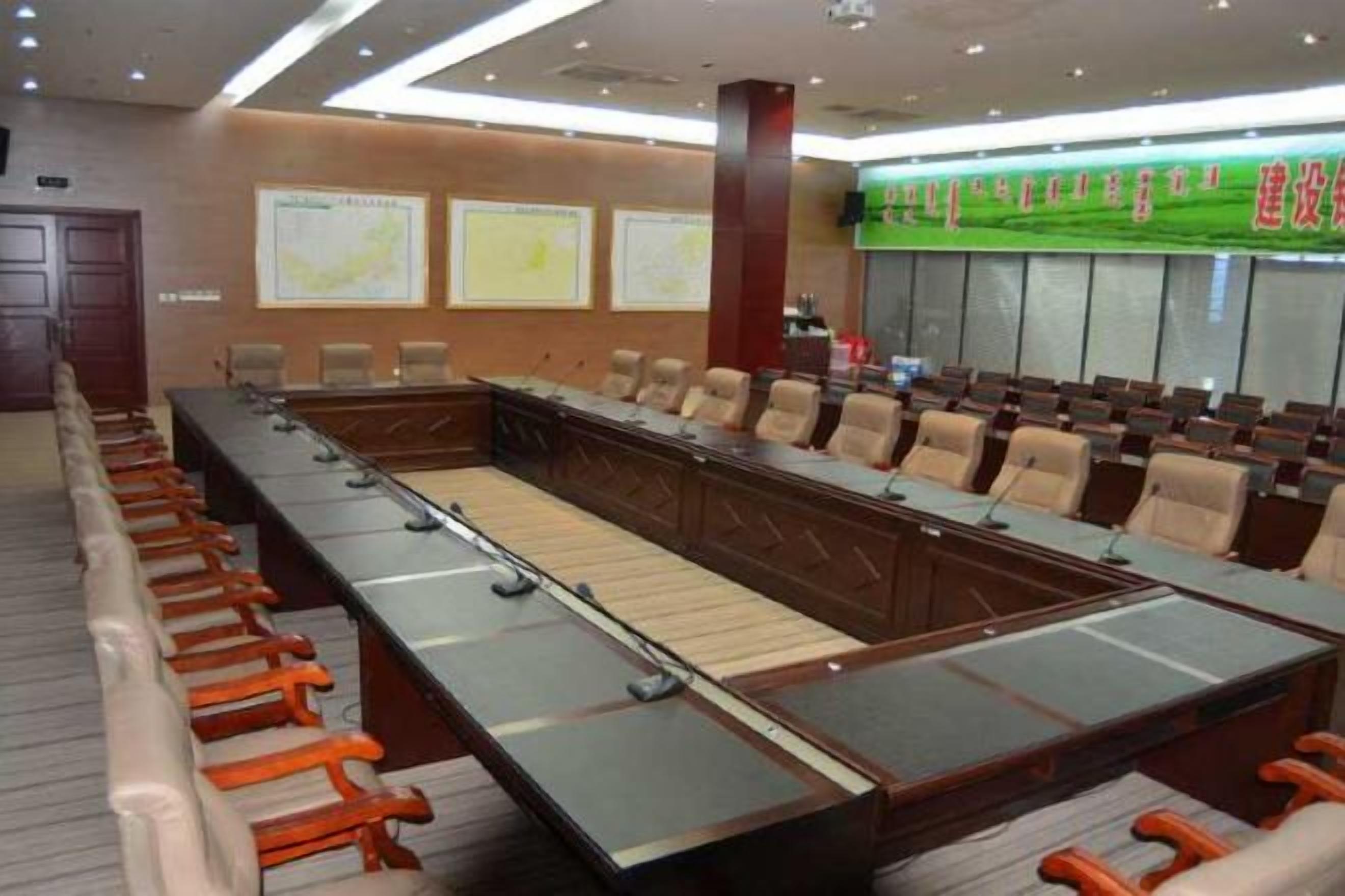 A conference room with a long table and multiple chairs, a large screen, and a map on the wall.