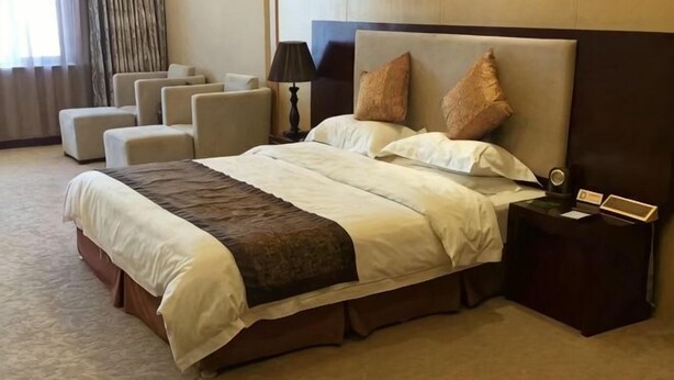 Une chambre d’hôtel avec un grand lit, une table de chevet avec une lampe, une petite table avec un livre et une fenêtre avec des rideaux.