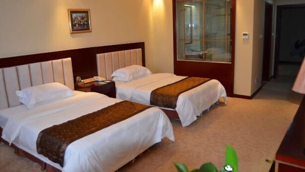 Ein Hotelzimmer mit zwei Betten, einem Nachttisch, einem Telefon und einem Fenster mit Jalousien.