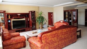 Ein Wohnzimmer mit einer Couch, Sesseln, einem Fernseher und einem Schrank.