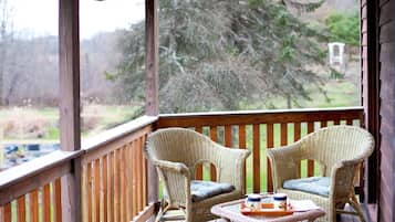 Une terrasse en bois avec deux fauteuils en osier et une petite table, donnant sur une zone boisée.