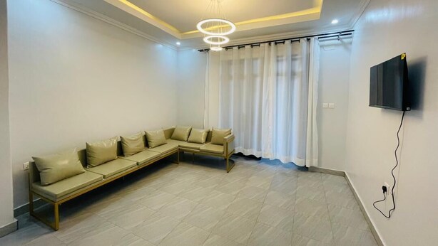 A modern living room with a sectional sofa, a flat-screen TV mounted on the wall, and a ceiling light fixture.