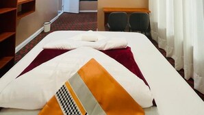 A hotel room with a bed, a desk, a chair, a wardrobe, and a bathroom visible through an open door.