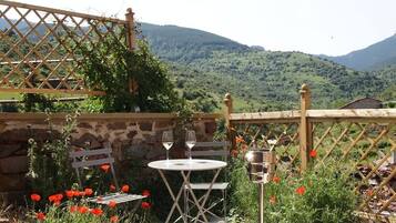 A patio with a table and chairs, a wine glass, and a metal container, surrounded by red poppies and a stone wall.
