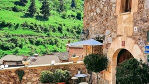 Ein Steinhaus mit einer kleinen Terrasse, Blumentöpfen und Blick auf grüne Hügel.