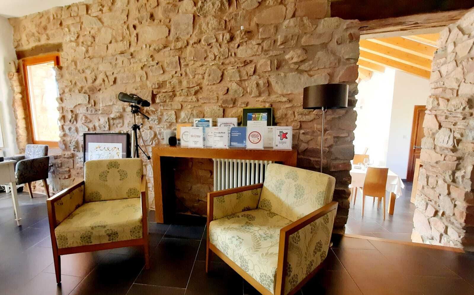 Une pièce chaleureuse aux murs de pierre, avec deux fauteuils, une table et une cheminée.