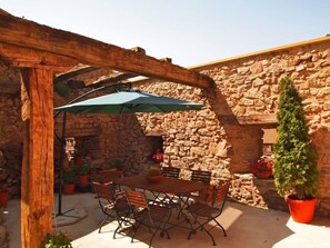 Um pátio externo com parede de pedra, pérgola de madeira e uma mesa com cadeiras.