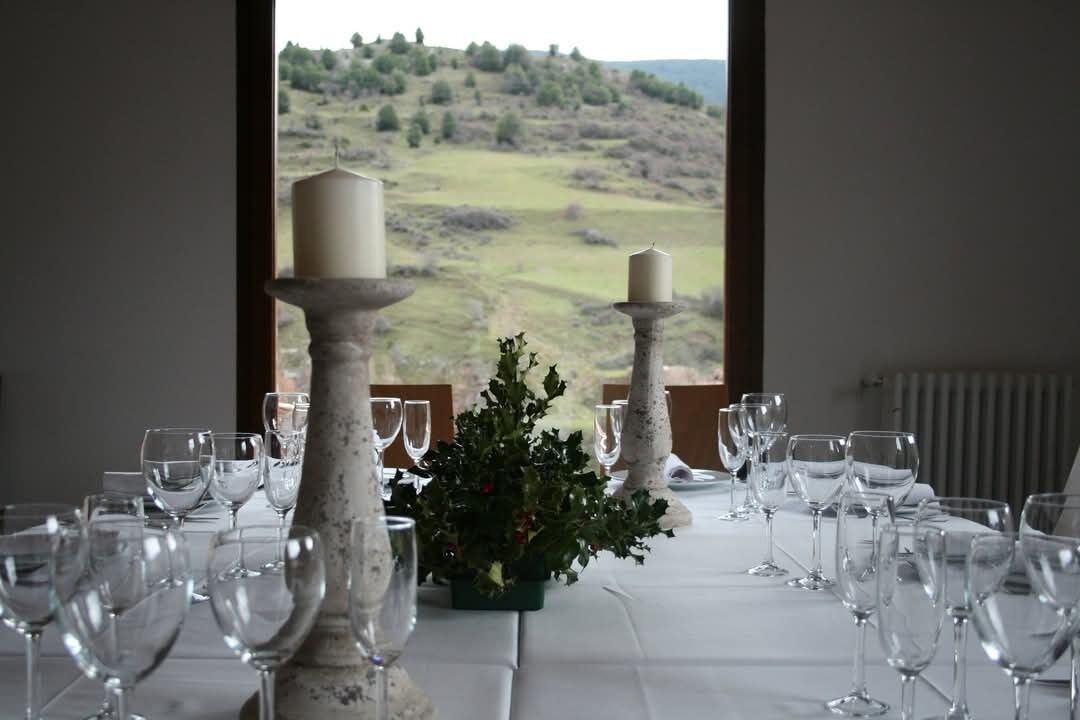 Taula preparada per a dinar, amb espelmes i una planta en test, amb vista a un paisatge idíl·lic.