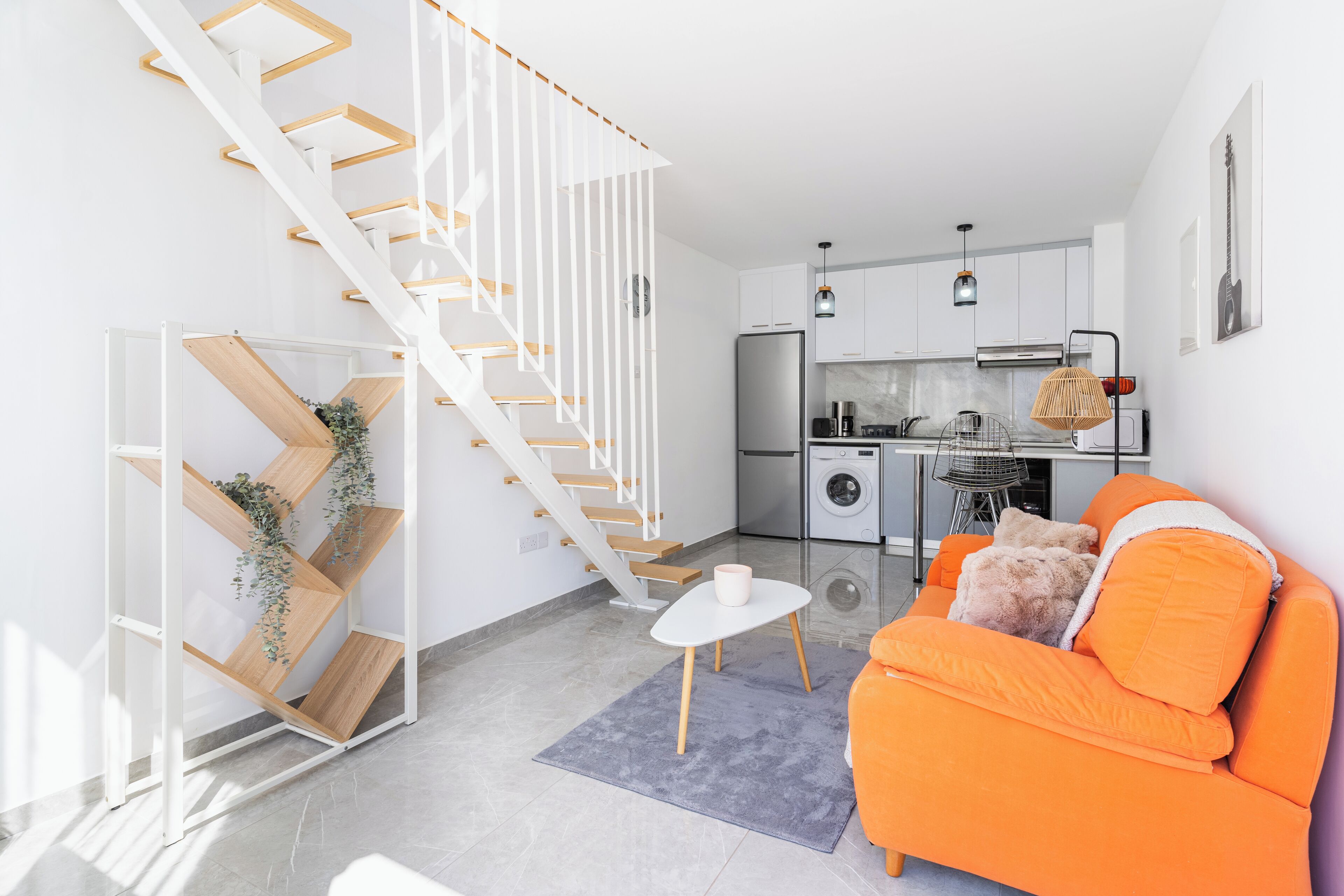 A modern living space with a staircase, kitchen, and orange sofa.