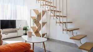 A modern living room with a TV, sofa, coffee table, and a unique wooden staircase. - Tangerine 1-Bedroom Apartment in Larnaca (Larnaca)