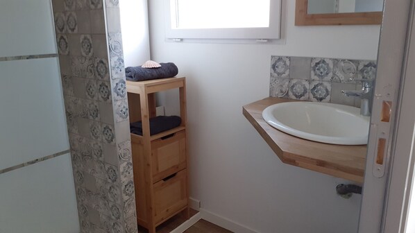 A small bathroom with a wooden shelf, a white sink, and patterned tiles.