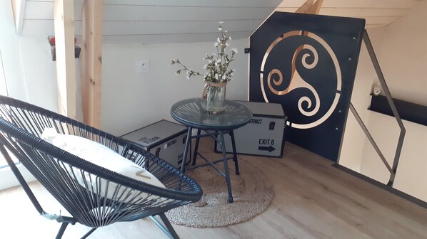 Una habitación con una silla negra, una mesita con un florero y una pieza decorativa grande en la pared.