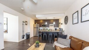 Eine moderne Küche mit dunklen Schränken, einer zentralen Kochinsel und Barhocker. Es gibt einen Holztisch mit Pflanze, ein Ledersofa mit gestreiften Kissen und ein gerahmter Spruch an der Wand.