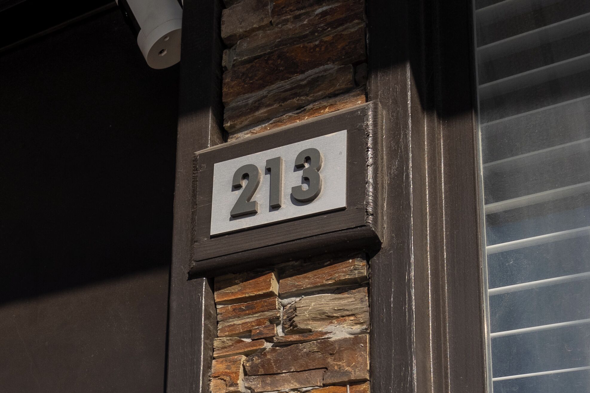 A house number '213' mounted on a stone and wood wall.