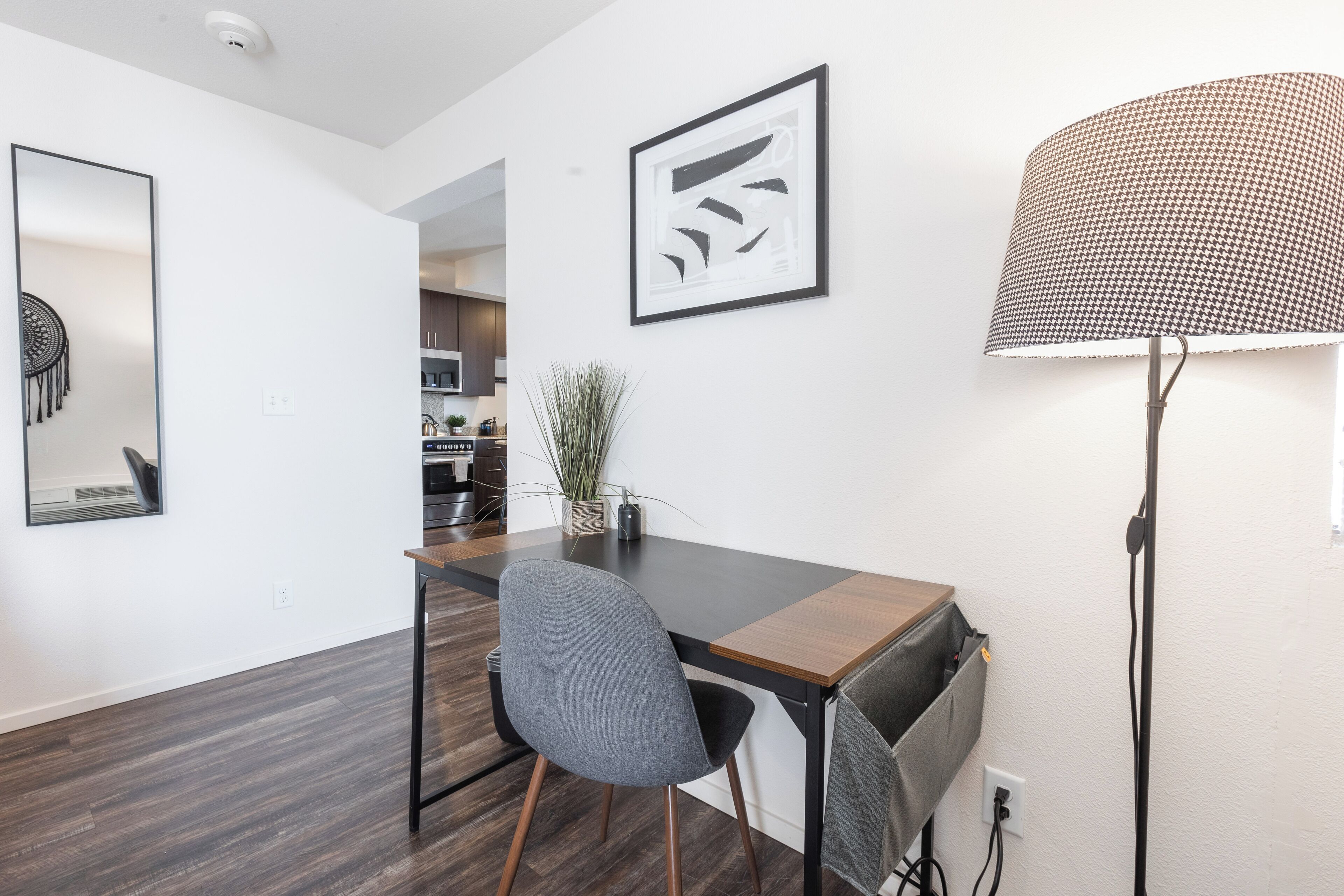 A modern kitchen with dark wooden flooring, a dining area with a dark table and grey chair, and a large floor lamp.