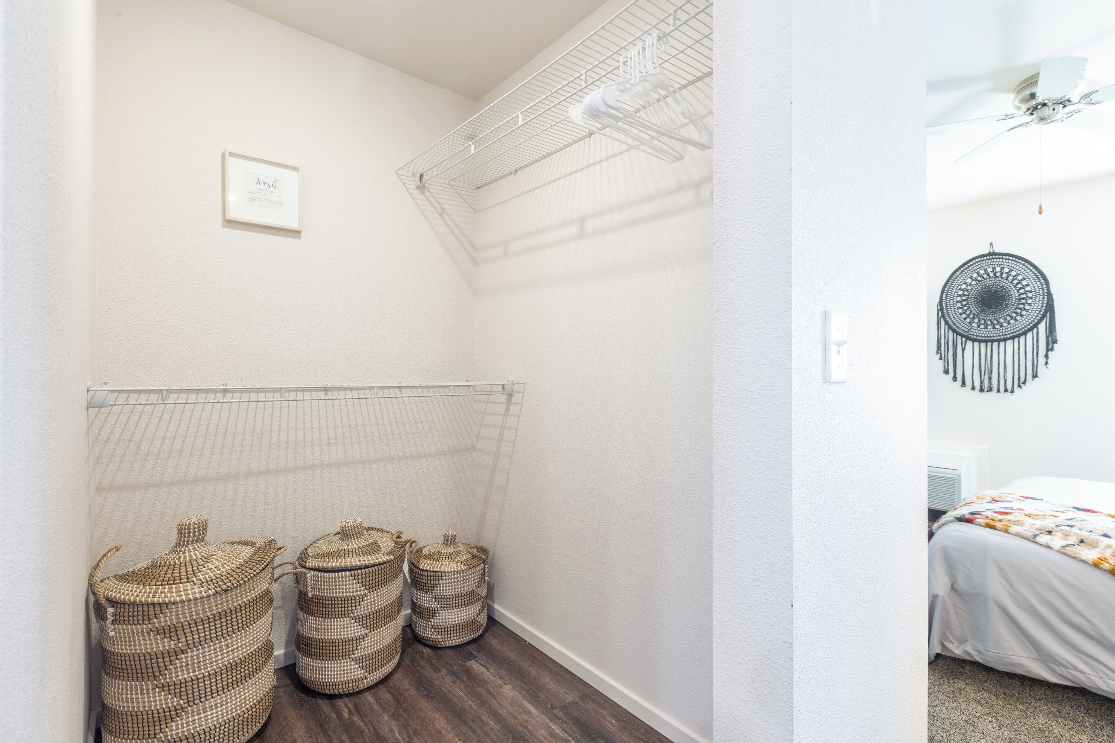 Un couloir avec un mur blanc, un ventilateur de plafond et un lit recouvert d’une couverture colorée dans la pièce adjacente.