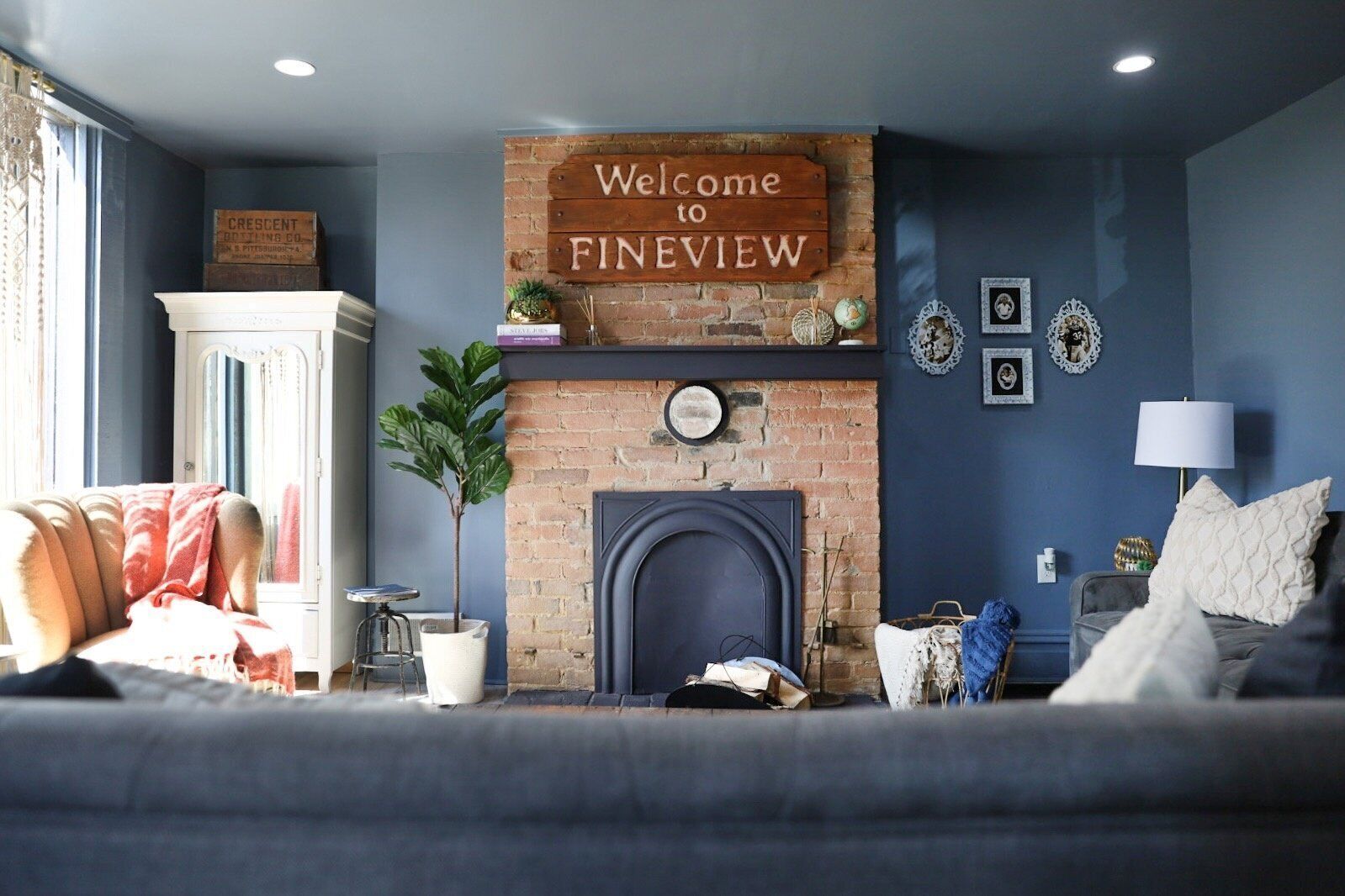 A cozy living room with a brick fireplace, a blue wall, and a 'Welcome to Fineview' sign.