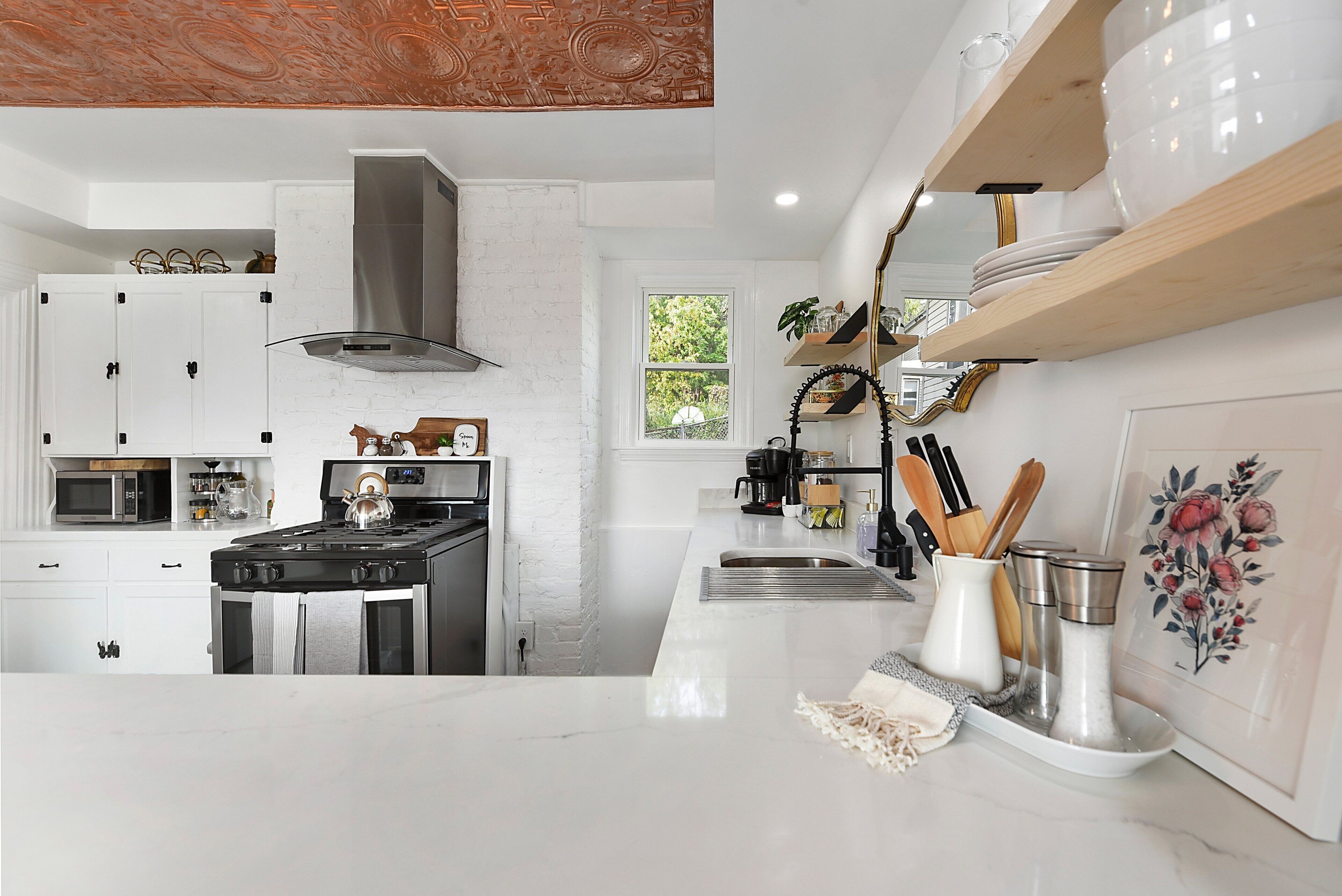 Una cocina moderna con muebles blancos, electrodomésticos de acero inoxidable y estantes de madera.