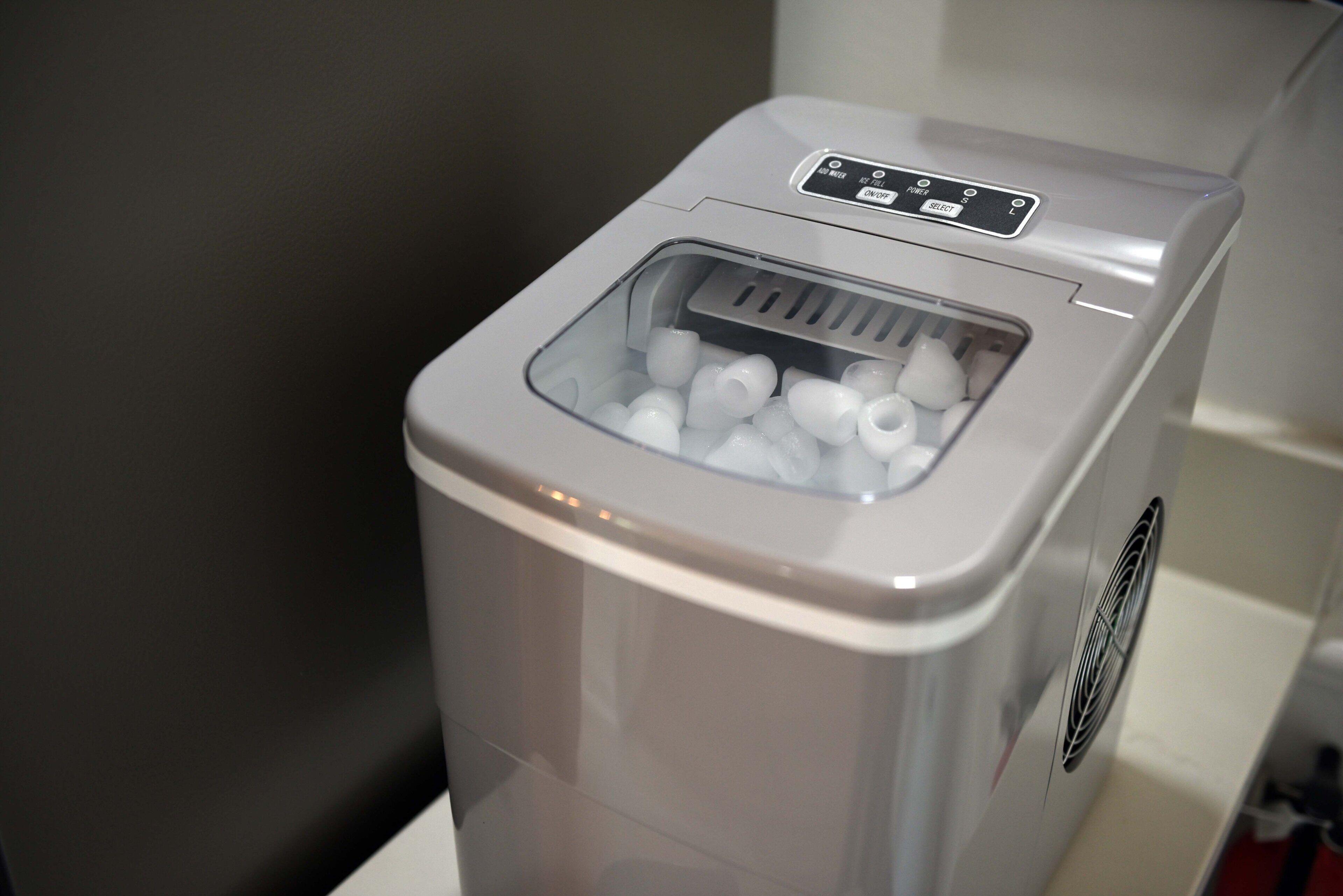 Un electrodoméstico compacto y moderno, de color blanco, con un panel de control y un compartimento transparente que contiene objetos blancos.