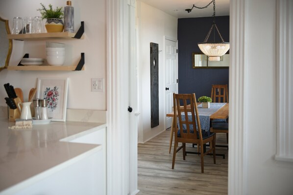 A kitchen with wooden shelves, a dining area with a table and chairs, and a hanging light fixture. - Yinz Retreat, Above the City Home (Pittsburgh)
