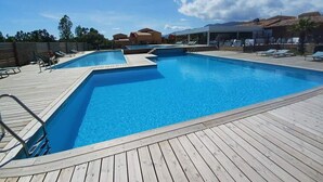 A swimming pool with a wooden deck, lounge chairs, and a clear blue sky. - LECCI: T2 air-conditioned ground floor 5 minutes from the beach with 3 swimming pools (Lecci)