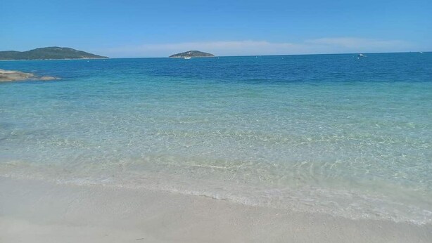 Une plage avec une eau claire et peu profonde, et des îles qui se dessinent à l’horizon.