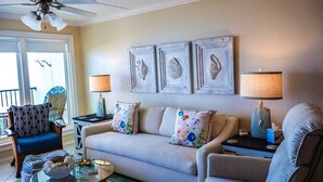 A living room with a sofa, armchairs, a coffee table, and decorative wall art. - Seville 602: Cozy 2-Bedroom Ocean View Condo (South Padre Island)