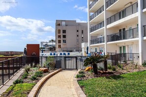 A gated entrance to a modern apartment building with a paved pathway leading to the gate.