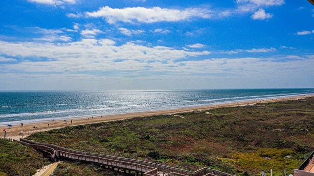 A coastal view with a beach, a wooden boardwalk, and a clear sky. - Seville 602: Cozy 2-Bedroom Ocean View Condo (South Padre Island)
