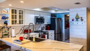 A modern kitchen with white cabinets, a stainless steel refrigerator, a microwave, and a sink. - Seville 602: Cozy 2-Bedroom Ocean View Condo (South Padre Island)