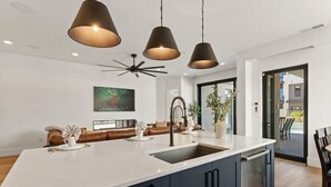 A modern kitchen with a large island, dark cabinetry, pendant lighting, and a view to the outside. - The Castle 8 Bedroom Home (St. George)
