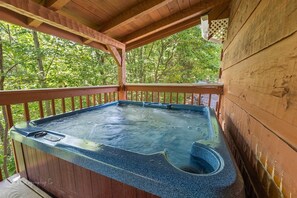 Relax in a hot tub on a shaded outdoor deck surrounded by lush greenery.