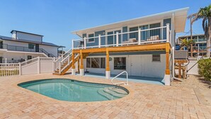 Una casa de dos pisos con piscina, un porche cubierto y una escalera que lleva al piso superior.