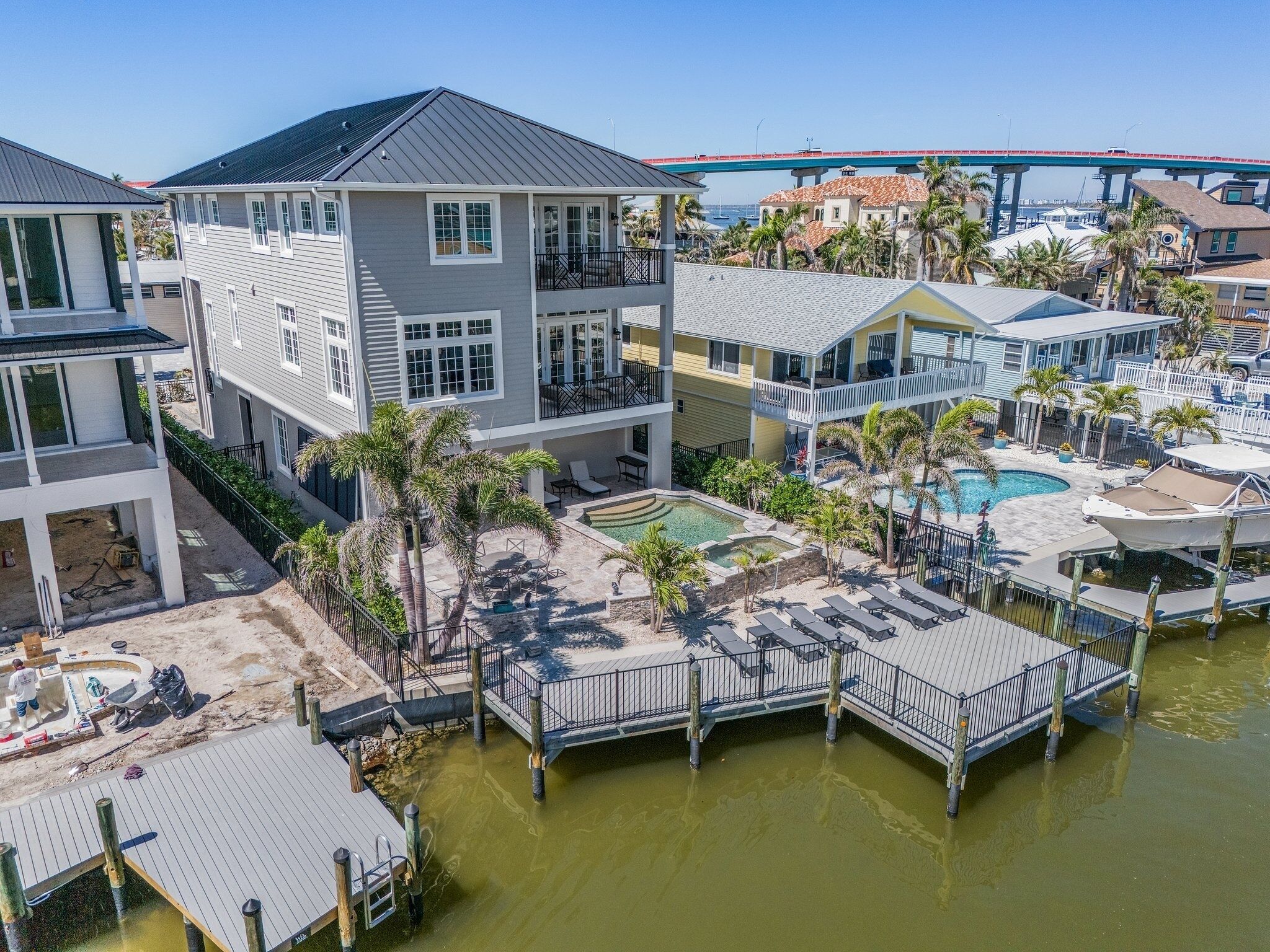 A multi-story residential building with a pool area, including a hot tub, lounge chairs, and a dock extending into a body of water.