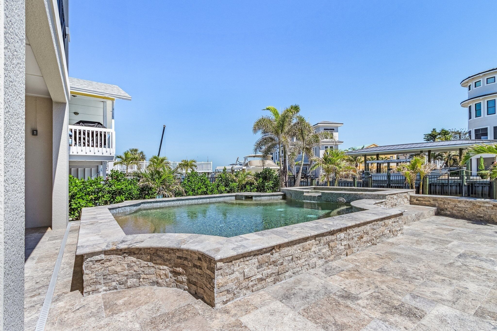 A pool area with stone steps and a clear pool, surrounded by greenery and modern buildings.