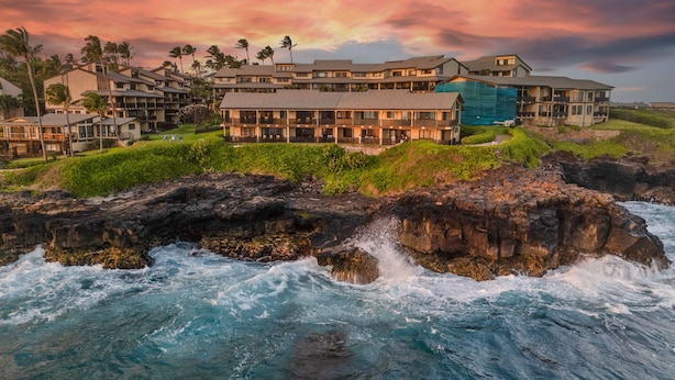 A coastal hotel with multiple buildings, a rocky shoreline, and waves crashing against the rocks. - Kauai Makahuena 4202 2 Bedroom Condo (Koloa)