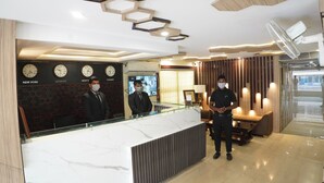 Zona de recepción de un hotel con mostrador de mármol, relojes que muestran nombres de distintas ciudades y un diseño de techo moderno.