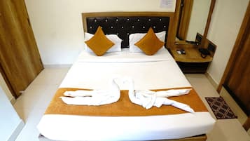 A neatly made bed with a headboard, two pillows, and towels arranged to resemble swans on a brown bed runner.