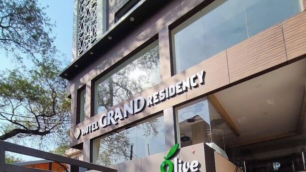 Un hotel llamado "HOTEL GRAND RESIDENCY" con un diseño moderno, que cuenta con una entrada destacada con una puerta azul y una escalera que conduce a la entrada.