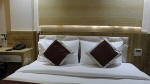 A hotel room with a wooden headboard, white bedding, and a bedside table with a telephone. - Hotel Milona (Navi Mumbai)