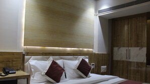 A hotel room with a bed, wooden headboard, bedside table with a phone, and a wardrobe with a marble panel. - Hotel Milona (Navi Mumbai)