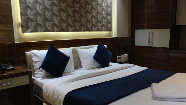 A hotel room with a neatly made bed, a bedside table with a phone, and a wardrobe with two doors. - Hotel Milona (Navi Mumbai)