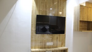 A modern room with a wooden wall unit, a flat-screen TV, and a built-in shelf. - Hotel Milona (Navi Mumbai)