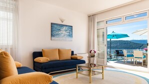 Een moderne woonkamer met een blauwe bank, een glazen salontafel en uitzicht op een balkon met tuinmeubels.