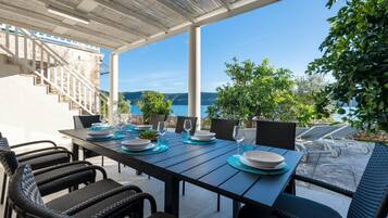 Un espace extérieur aménagé pour les repas, avec vue sur la mer, un escalier et une pergola.